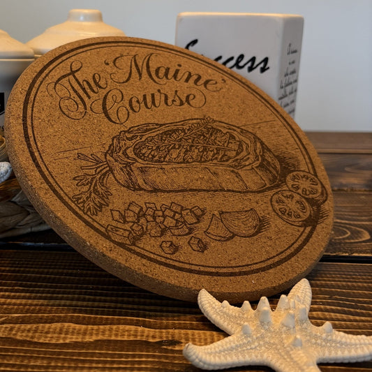 Kurken pannenonderzetter, gegraveerd met een gerecht en de tekst The Maine Course, rechtop op een houten tafel