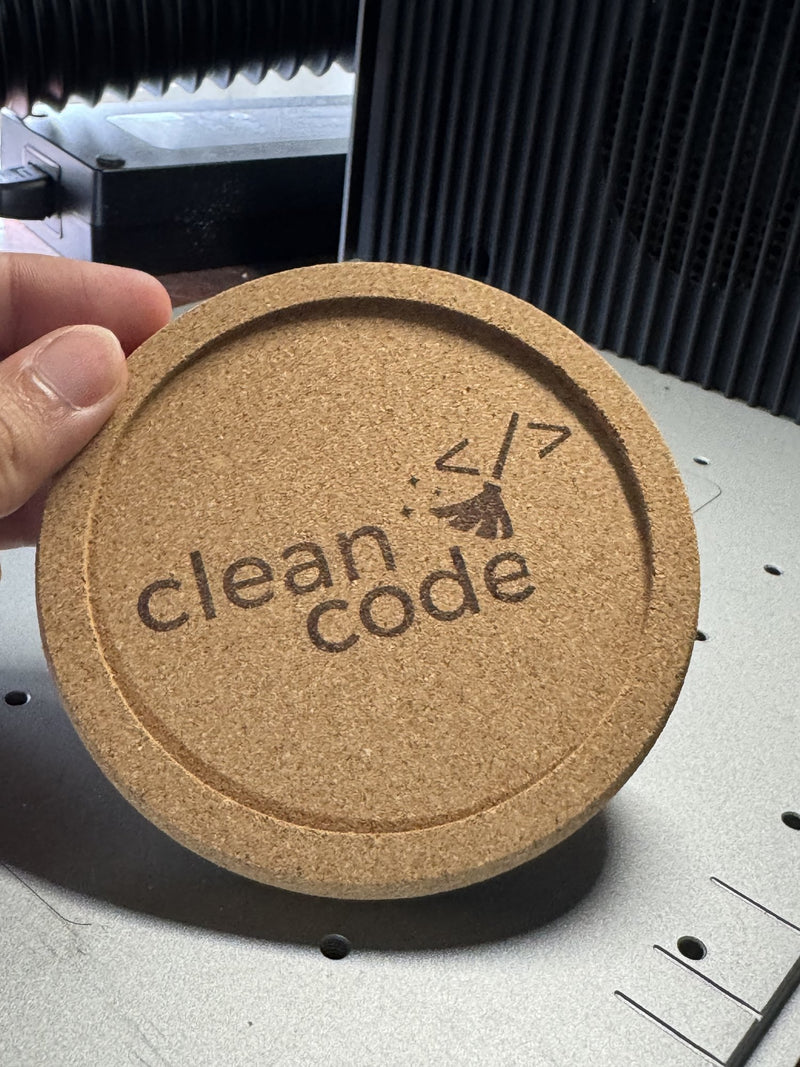 Kurken onderzetter met opstaande rand, gegraveerd met een eigen logo, in de hand bij de lasergraveermachine