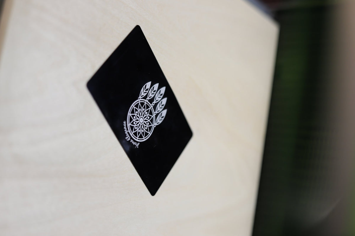 Zwart metalen visitekaartje met een gegraveerd dromenvanger-logo en de tekst Home Elegance, schuin op een houten ondergrond