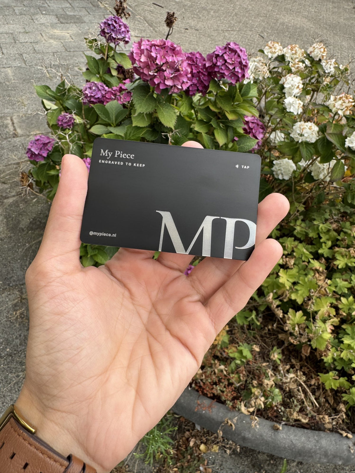 Zwart metalen visitekaartje met een gegraveerd MP-monogram en een tap-symbool, in de hand